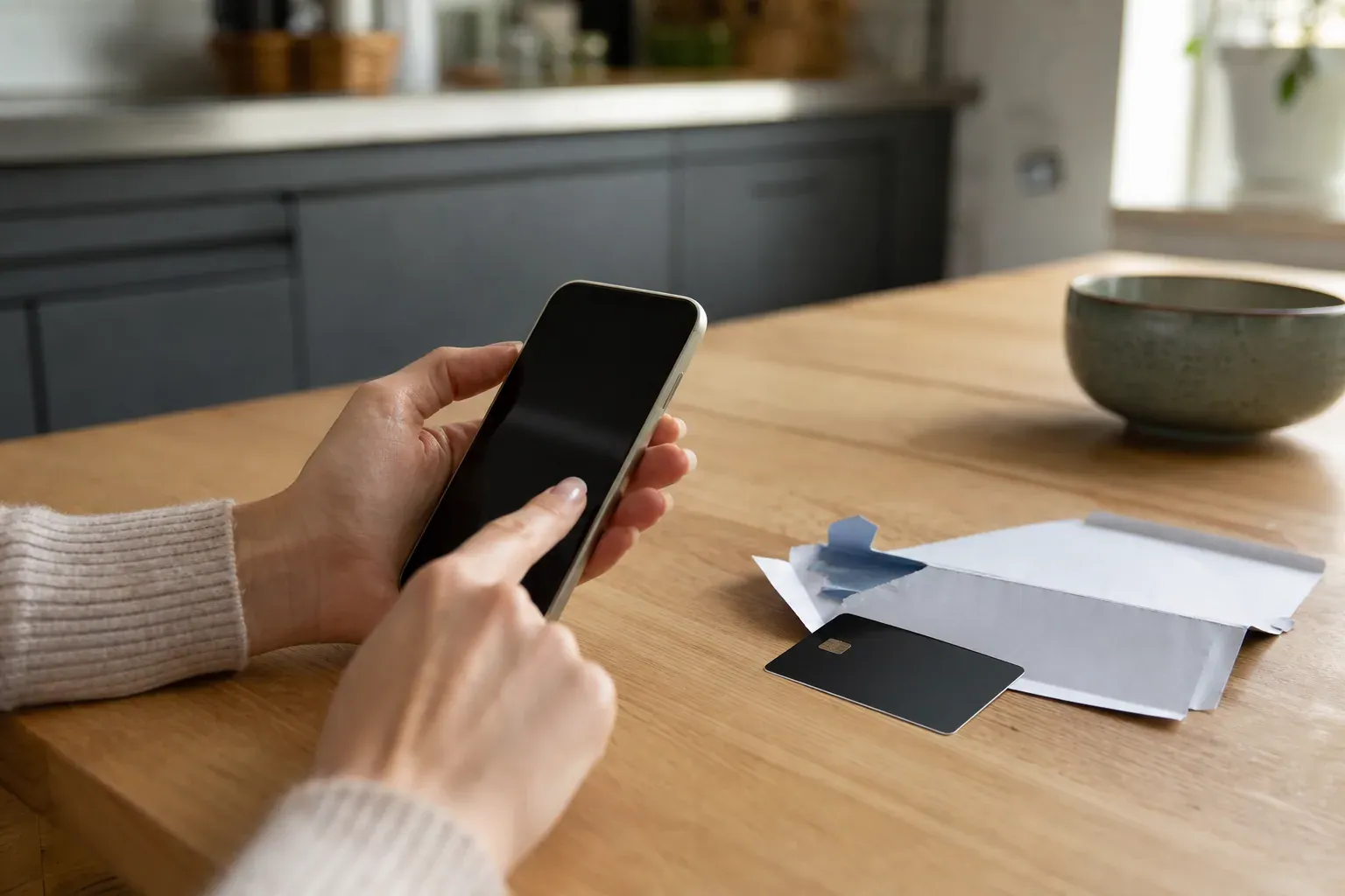 Photo réaliste d’une personne activant une carte bancaire neuve sur son smartphone, avec la carte et l’enveloppe du code secret posées sur une table.