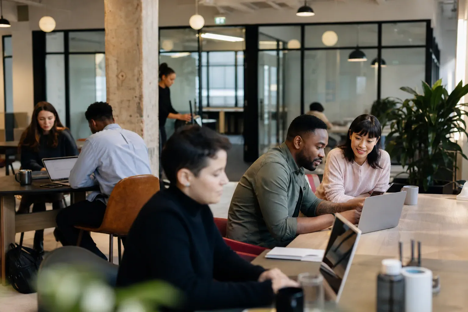 Équipe d’entreprise travaillant dans un espace de coworking moderne, en ambiance réelle, avec ordinateurs portables et salle de réunion vitrée.