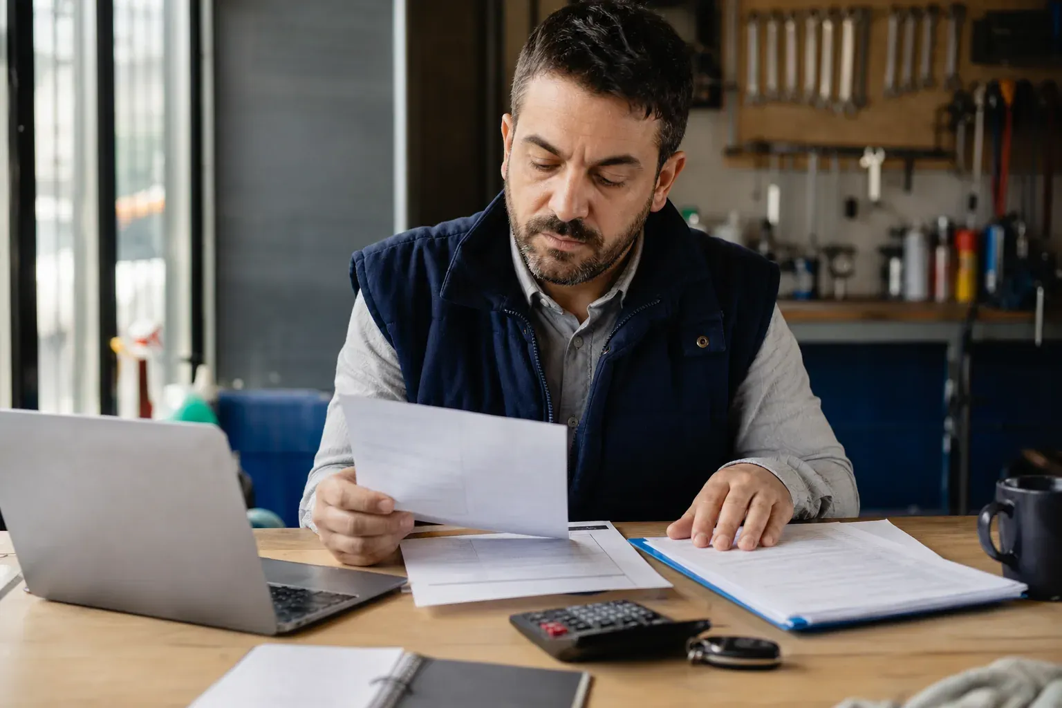 Une entrepreneure individuelle compare des contrats d’assurance professionnelle sur son bureau, avec documents, ordinateur et outils de travail.