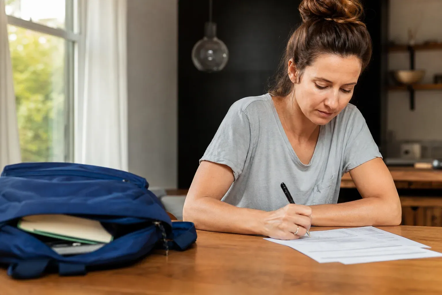 Parent remplissant un formulaire d'assurance scolaire à une table, cartable d'enfant posé à côté, ambiance rentrée scolaire, lumière naturelle.