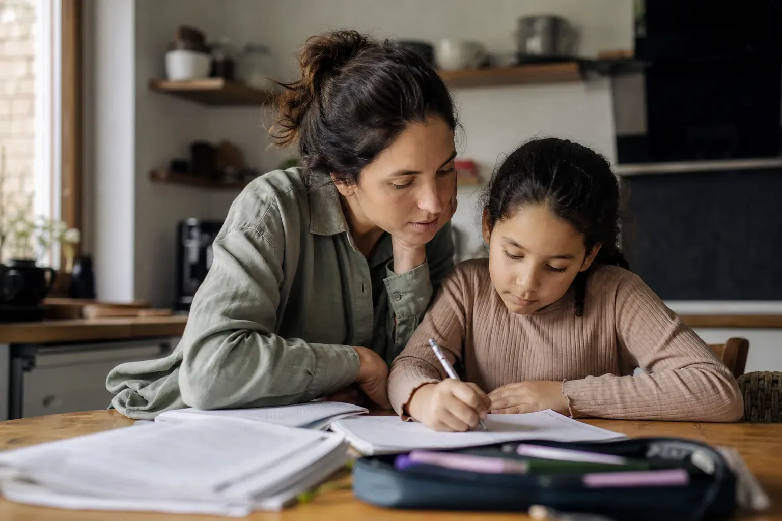 Un parent aide un enfant à faire ses exercices de mathématiques à la maison, autour d’une table bien éclairée avec cahiers et crayons.