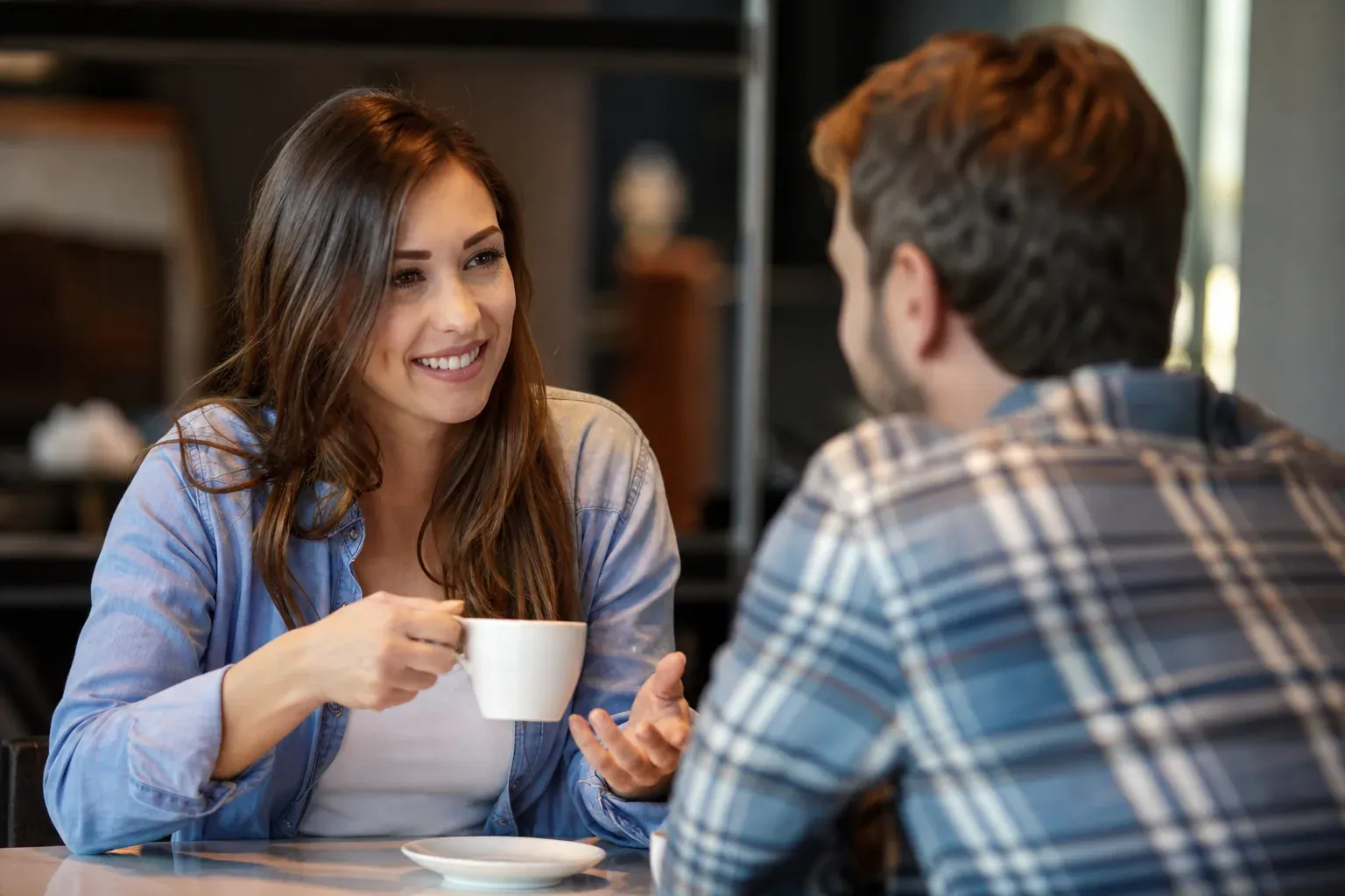 Deux personnes se parlent dans un café, avec une posture ouverte et un échange naturel et détendu.