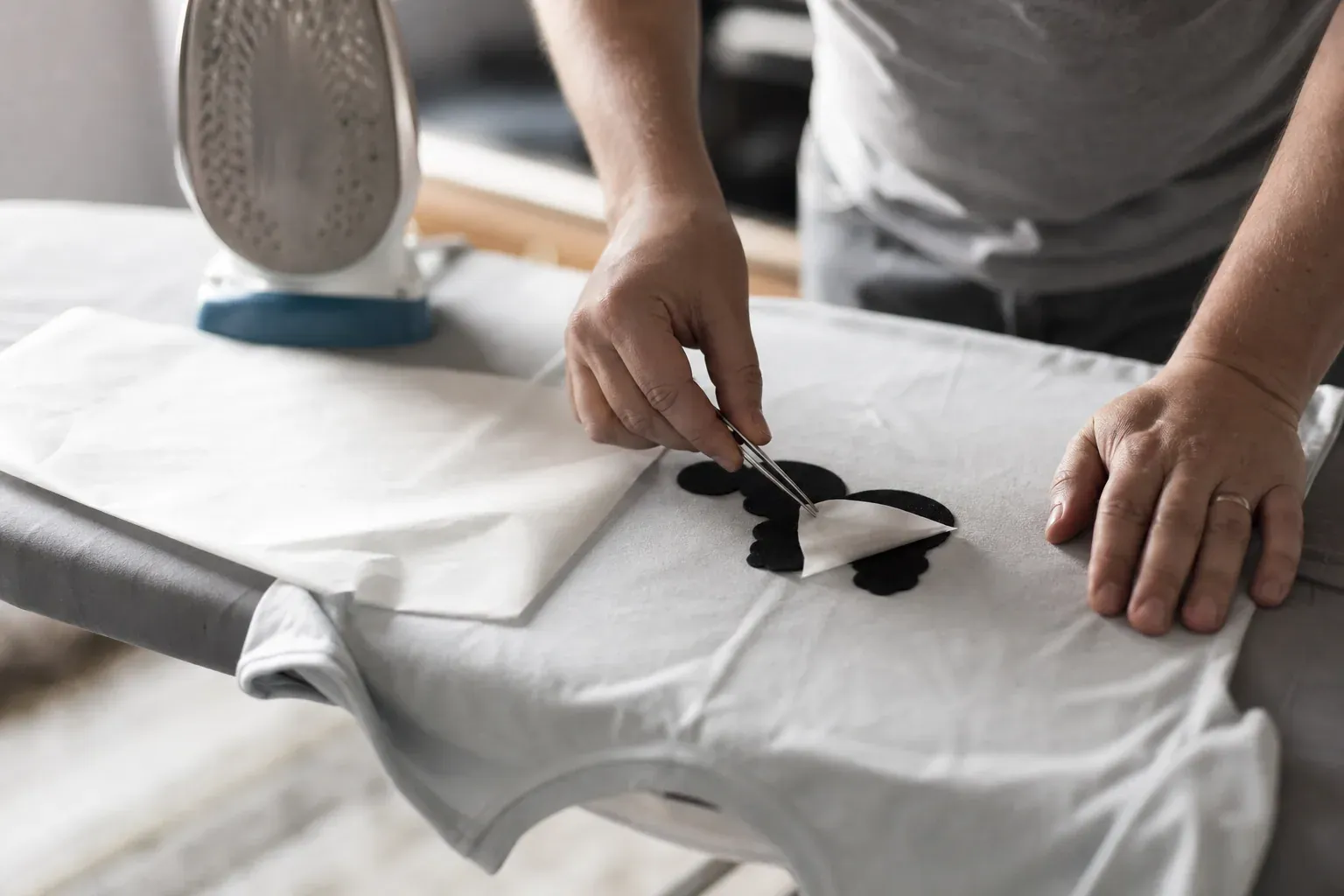 Gros plan réaliste d’une personne retirant prudemment un flocage d’un T-shirt en coton avec un fer à repasser et du papier sulfurisé.