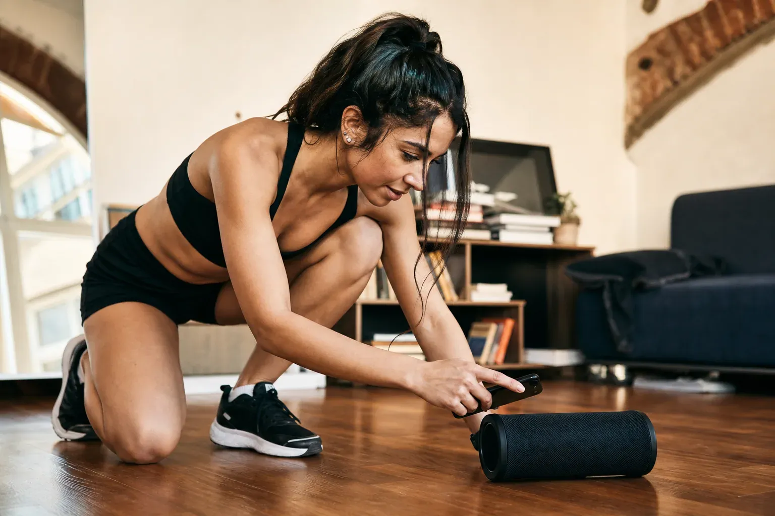 Une personne prépare une playlist sur son téléphone à côté d’une enceinte, dans un espace de danse lumineux avant une séance de workout.