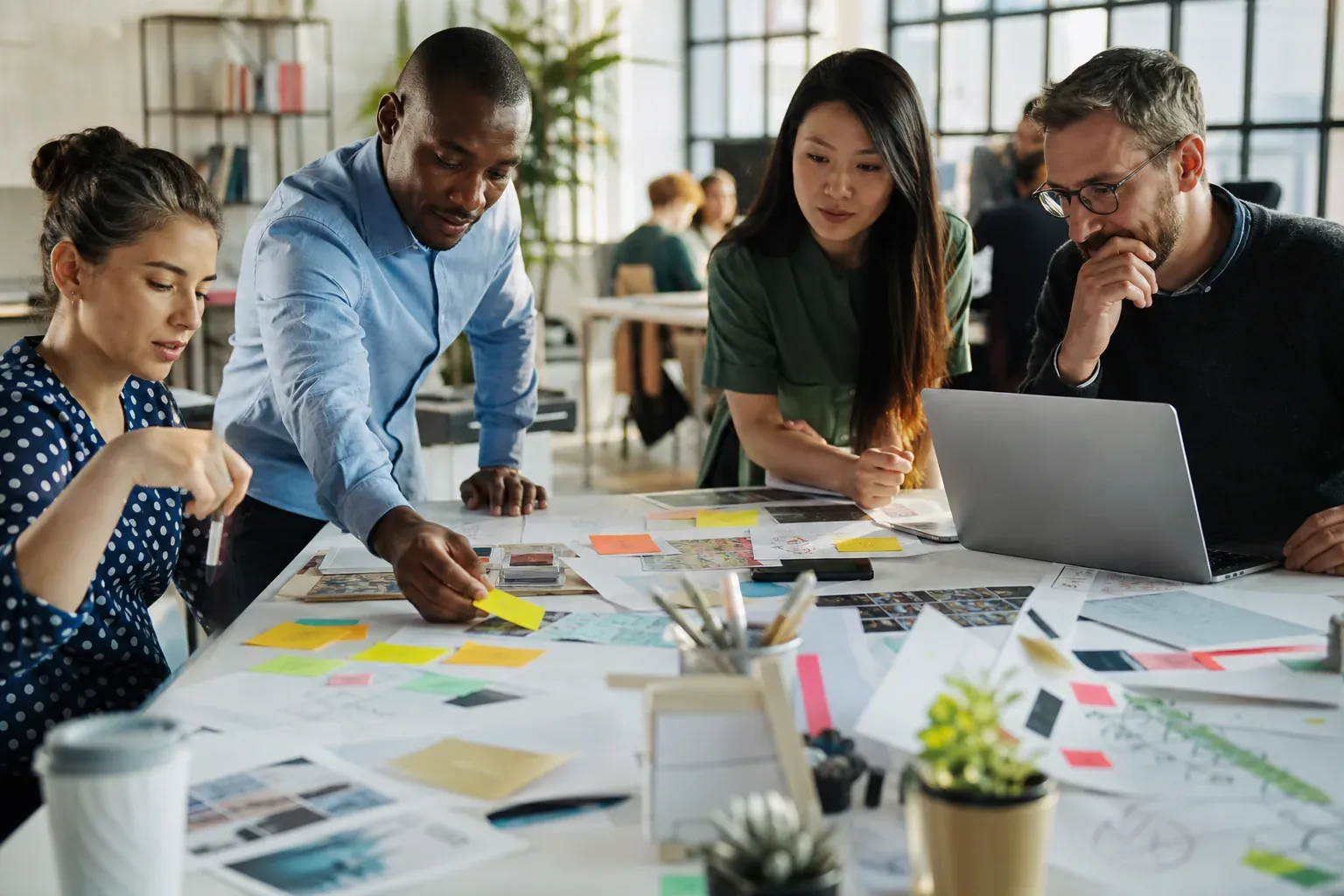 Une équipe diverse travaille autour d'une table couverte de post-it, d'ordinateurs et de canevas dans un espace de co-conception lumineux.