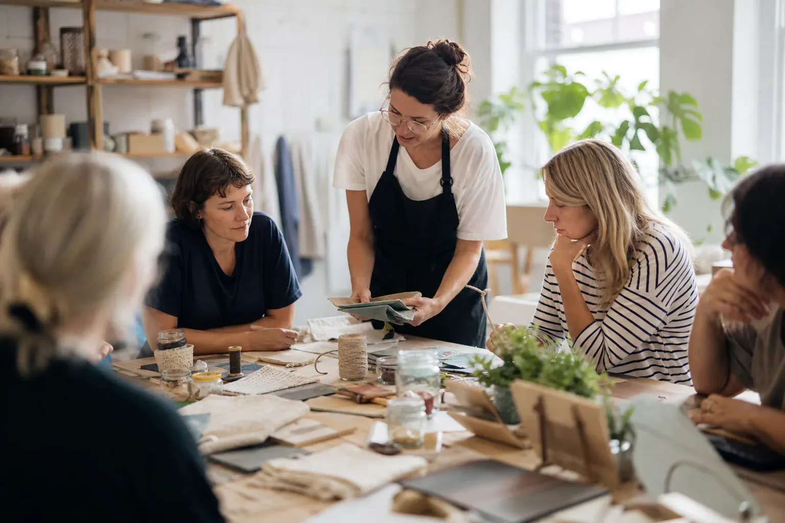 Un atelier DIY convivial avec un animateur au centre, des participants autour d’une grande table en bois et du matériel créatif éparpillé.