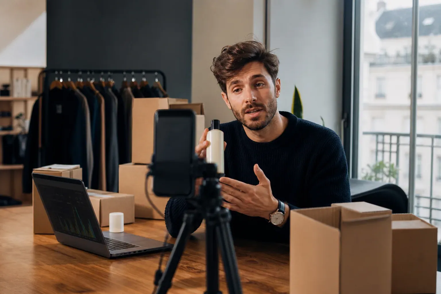 Un entrepreneur français filme une démonstration produit dans un petit studio lumineux, avec des colis et un ordinateur ouvert sur une boutique en ligne.