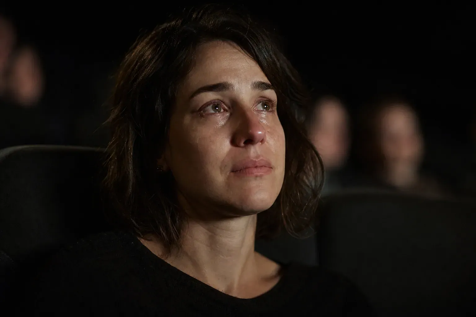 Une personne seule dans une salle de cinéma sombre, éclairée par la lumière de l’écran, dans une ambiance intime et émotive.