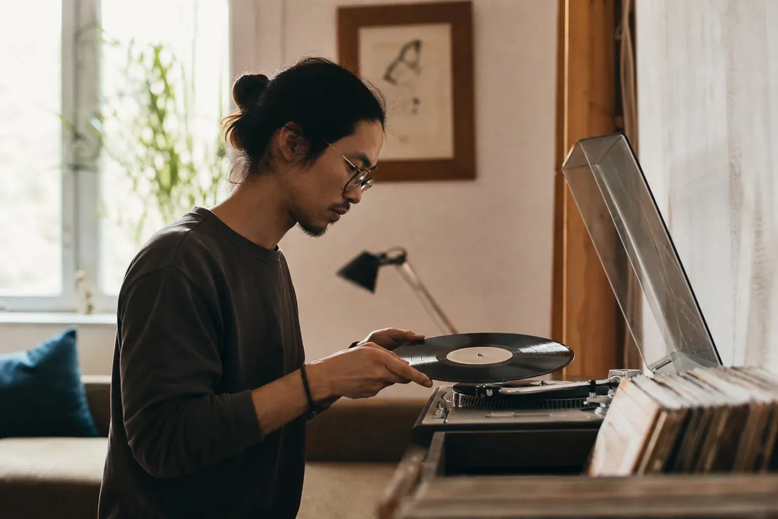 Une personne pose un disque vinyle sur une platine dans un intérieur chaleureux, avec des pochettes d’albums visibles autour.