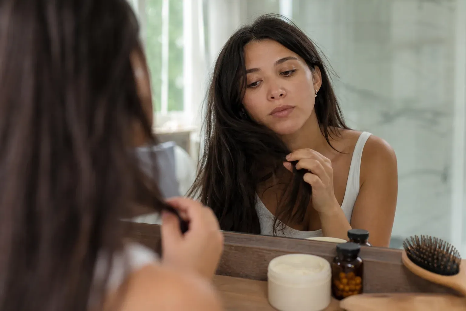 Photo réaliste d’une personne examinant des pointes de cheveux abîmées, avec des compléments capillaires et des soins sur une table.
