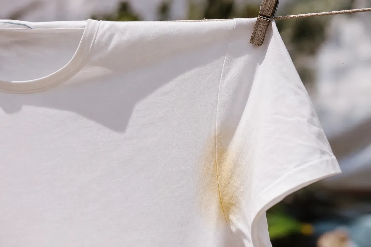 Un tee-shirt blanc étendu au soleil, avec une auréole jaunie visible sous l'aisselle, lumière naturelle.