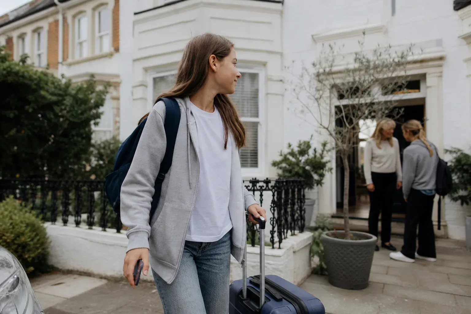 Un adolescent avec un sac à dos et une valise devant une école de langue en Angleterre, dans une rue résidentielle britannique.