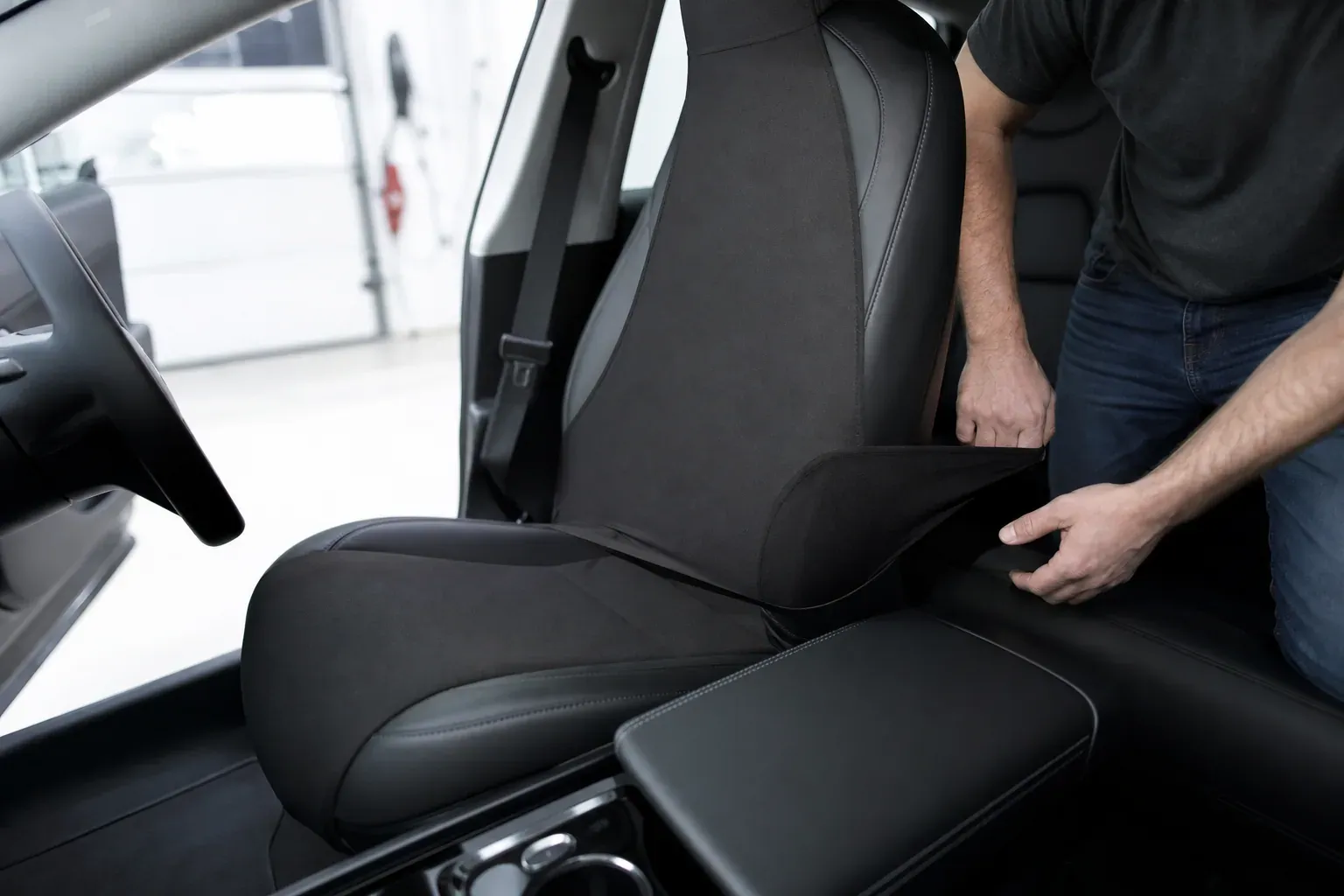 Gros plan sur l’intérieur d’une Tesla avec une housse de siège à bande élastique en cours de pose, dans un garage lumineux.