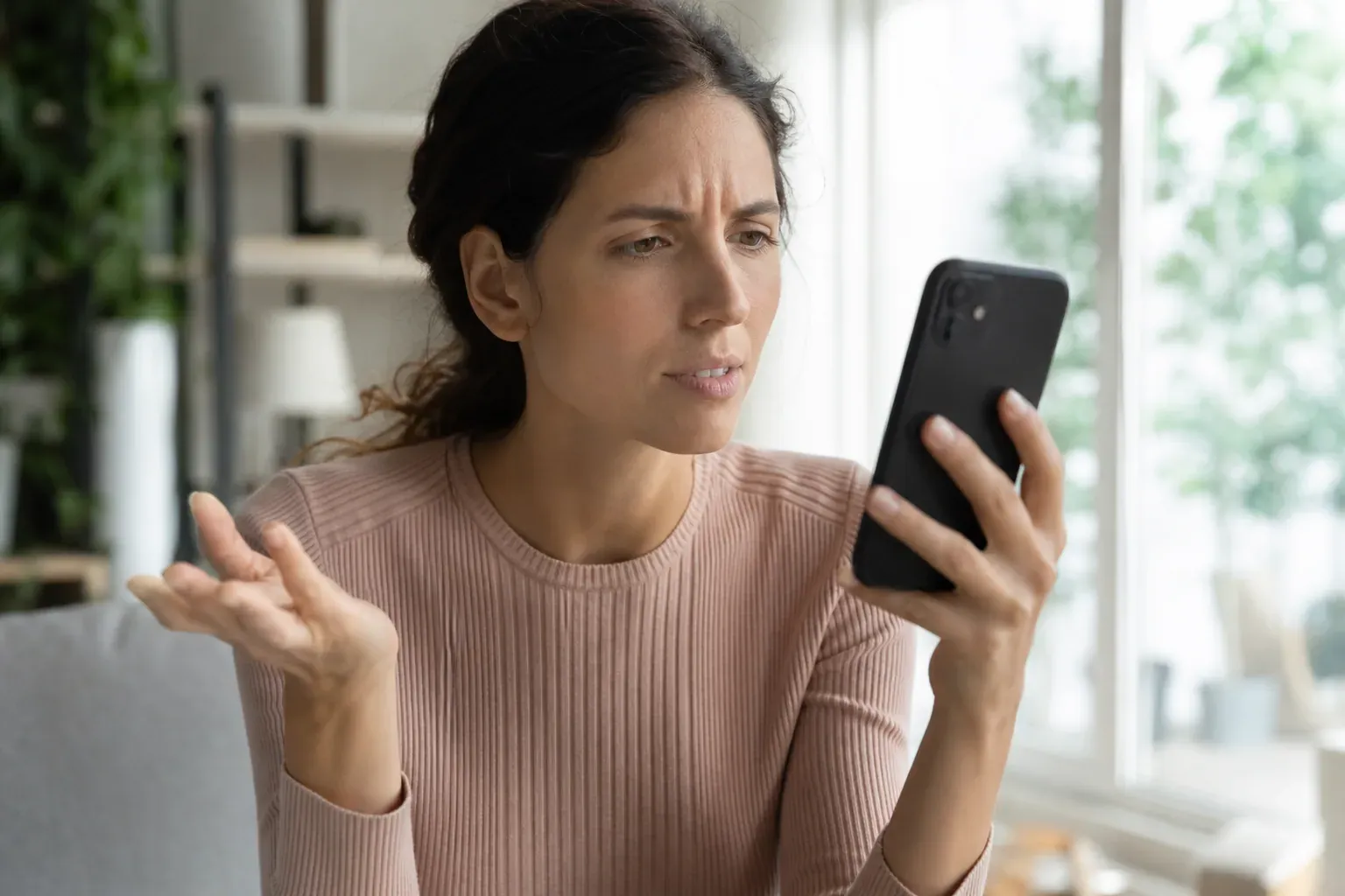 Personne tenant un iPhone et essayant d’utiliser Siri dans un intérieur lumineux, avec une expression de frustration.
