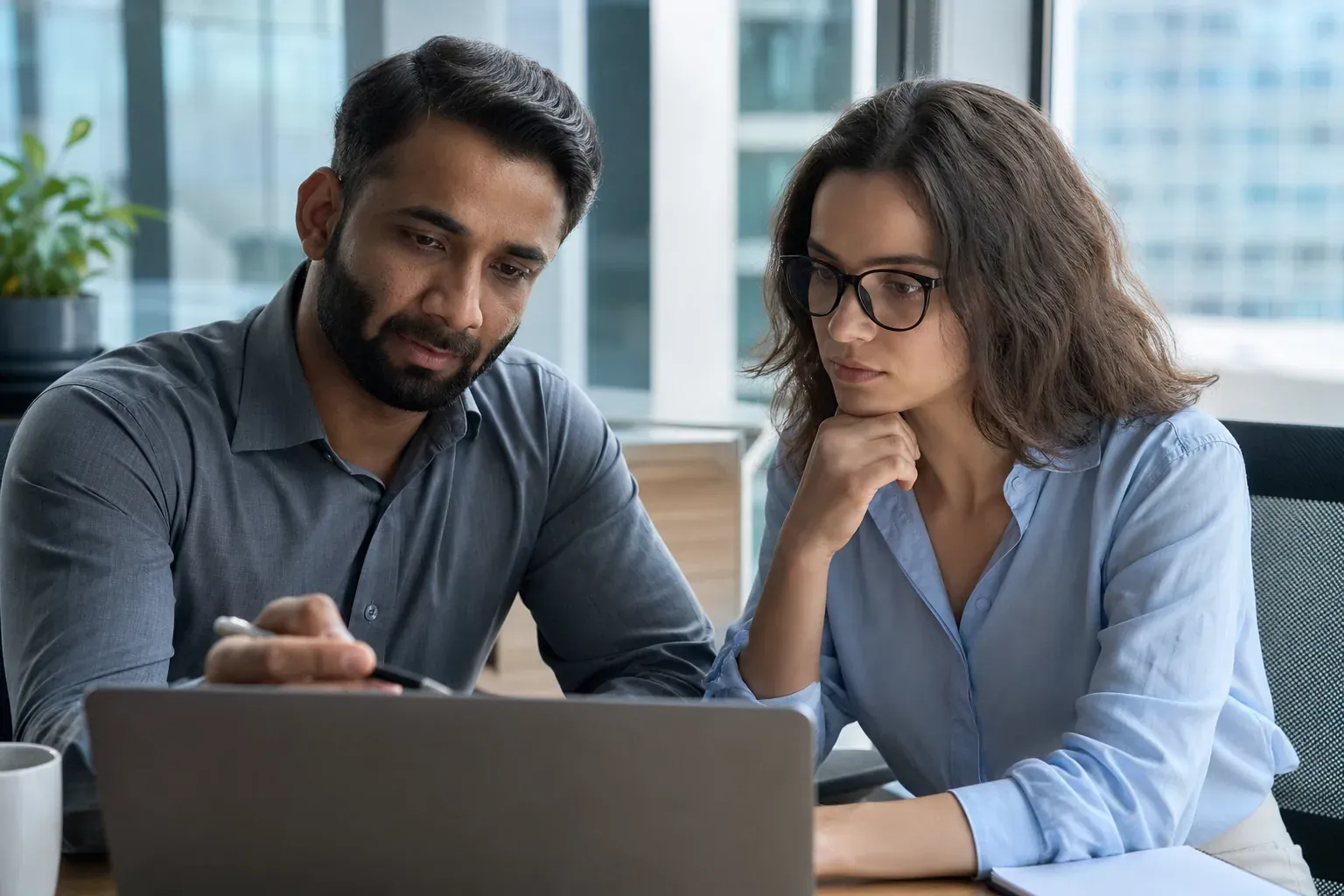 Deux personnes en séance de mentorat autour d’un ordinateur portable affichant des tableaux de bord de données dans un bureau moderne.