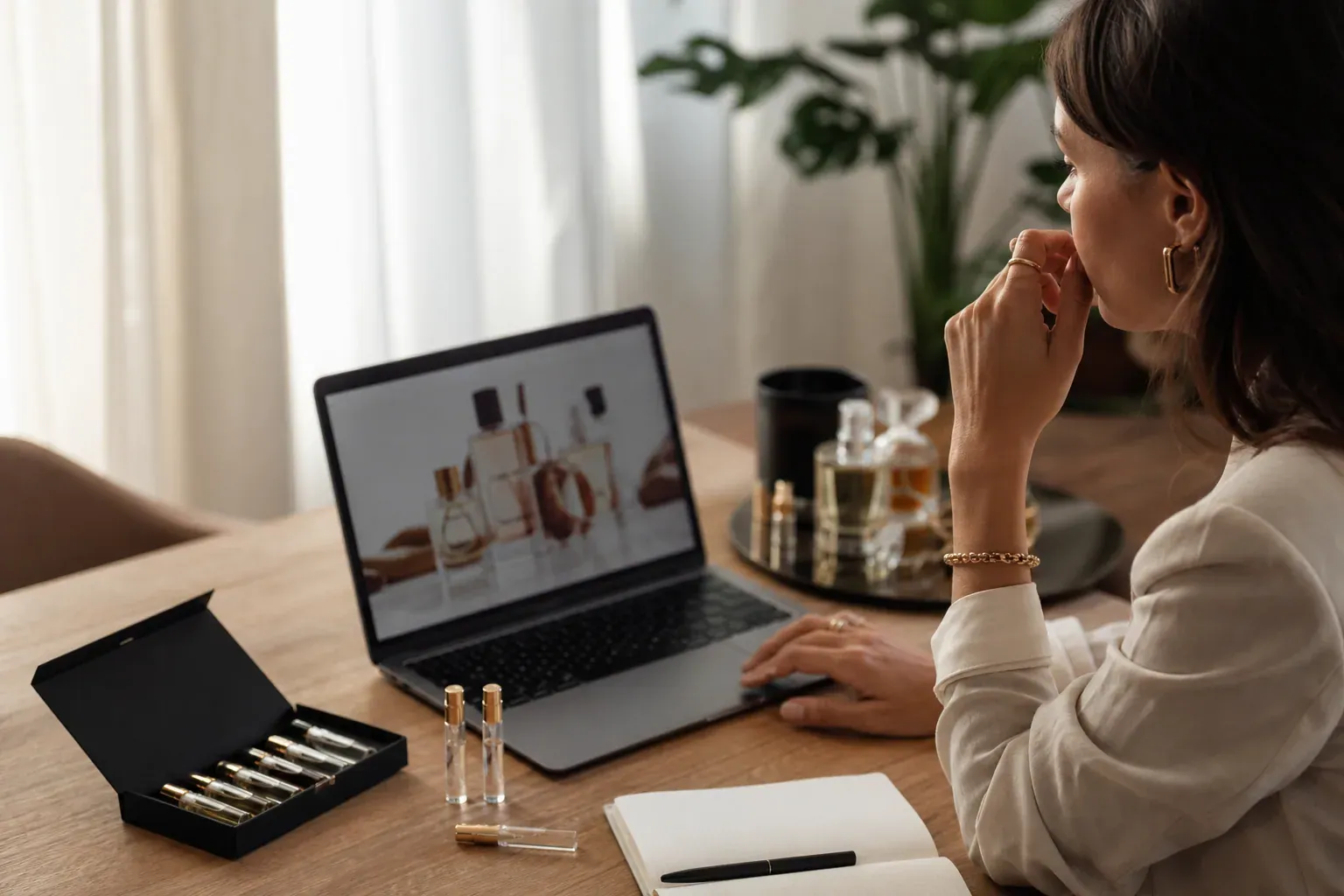 Personne à une table avec un ordinateur ouvert, des échantillons de parfum et un coffret découverte, dans une ambiance lumineuse et naturelle.