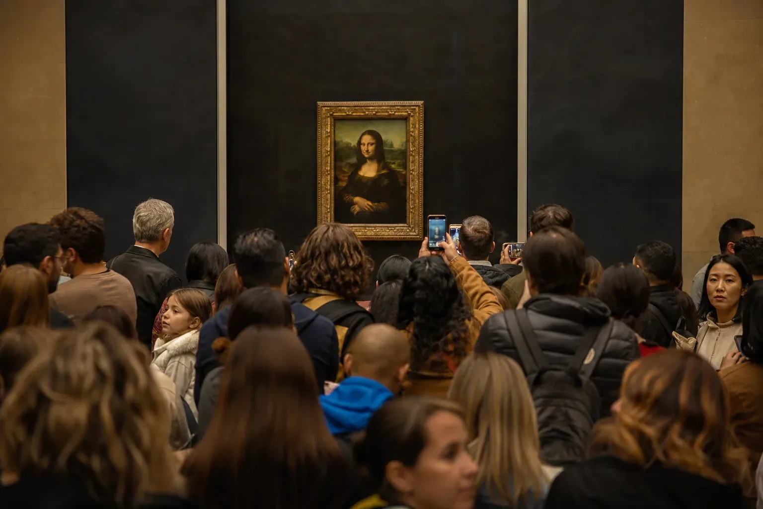 Des visiteurs du Louvre observent la Joconde derrière sa vitre de protection dans une salle de musée très fréquentée.