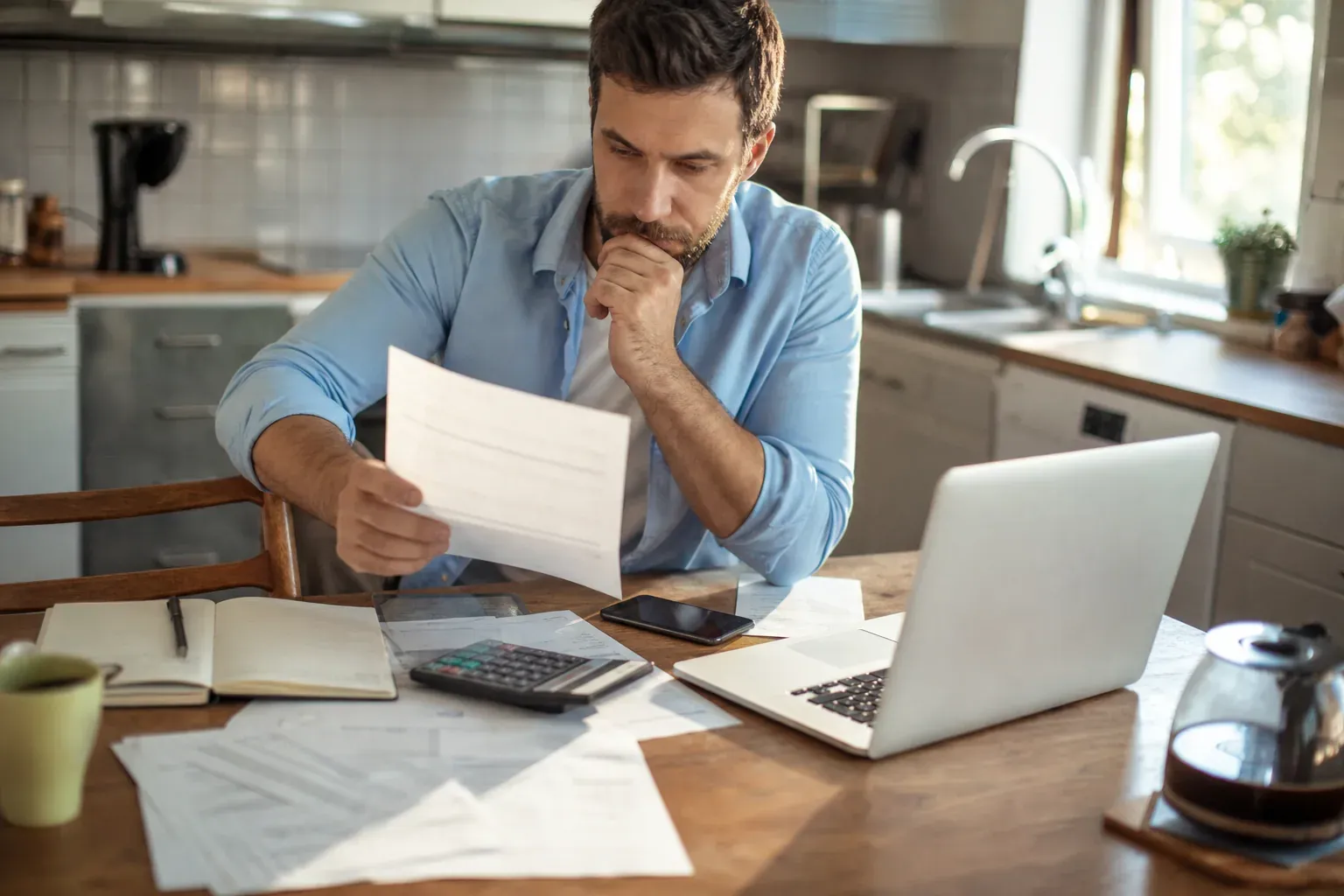 Personne comparant des offres de crédit sur un ordinateur portable, avec calculatrice et documents financiers sur une table.