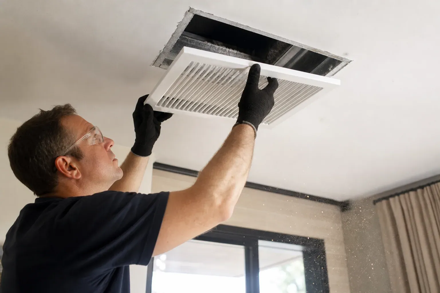 Un technicien nettoie une bouche de ventilation dans un intérieur moderne, avec des outils d’entretien et des éléments de réseau aéraulique visibles.