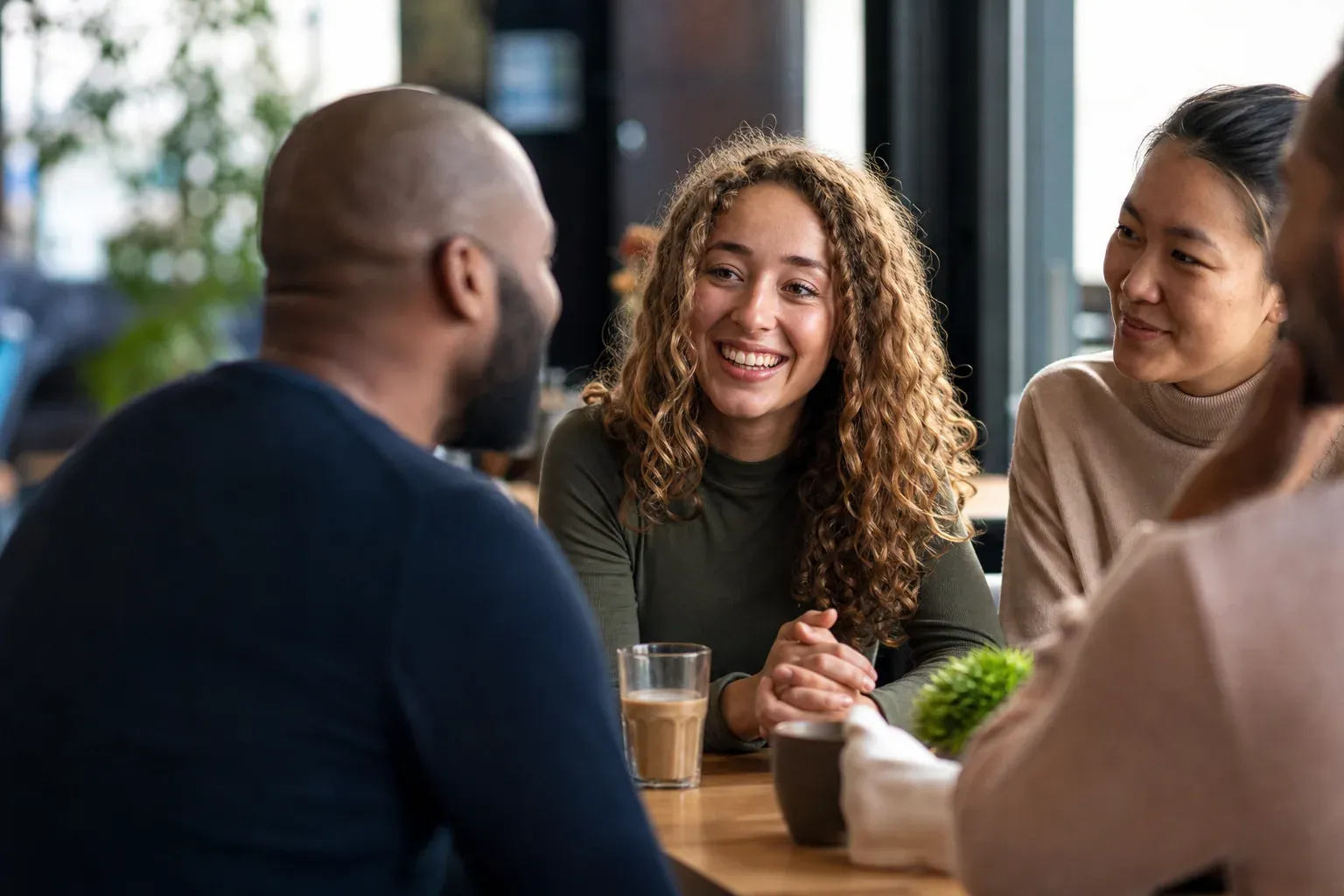 Photo réaliste d’un petit groupe de personnes en conversation bienveillante dans un café lumineux, avec une personne qui écoute attentivement.