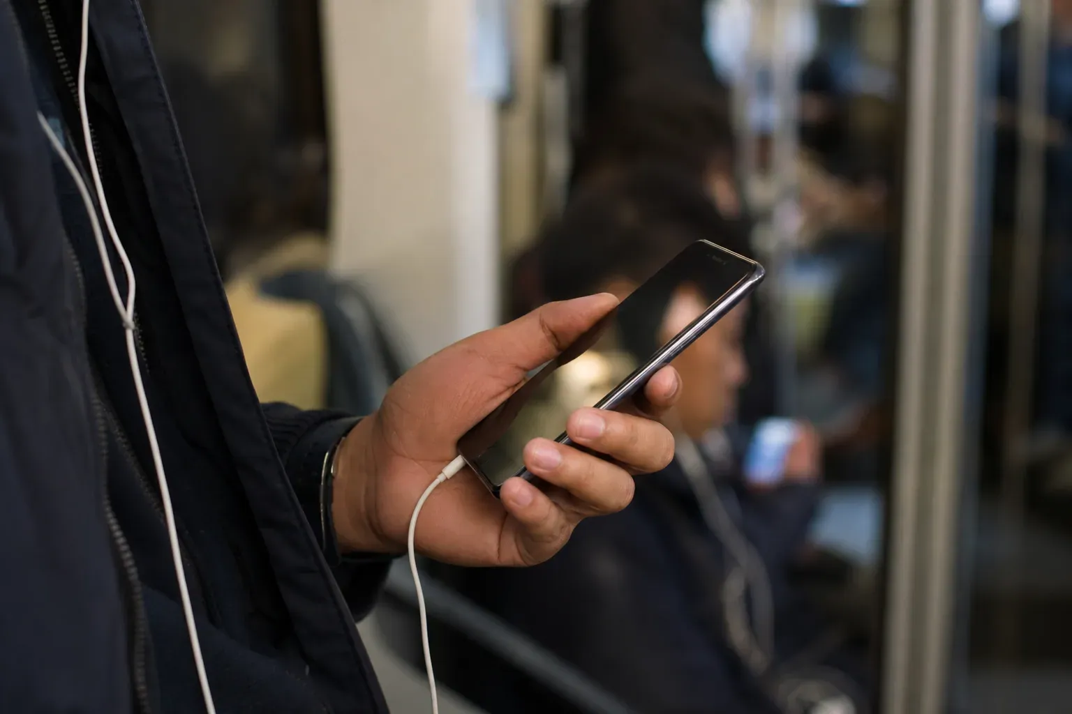 Une personne dans les transports écoute de la musique sur un smartphone pas cher avec des écouteurs filaires.