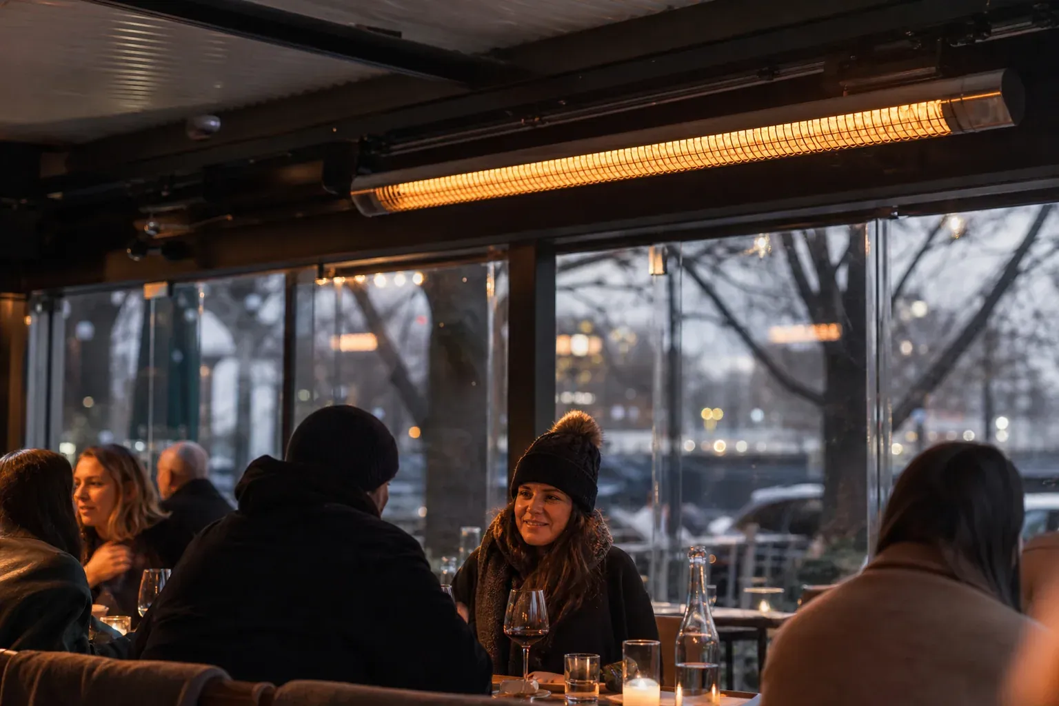 Terrasse de restaurant en soirée avec un tube radiant gaz fixé sous un auvent et des clients assis à proximité.