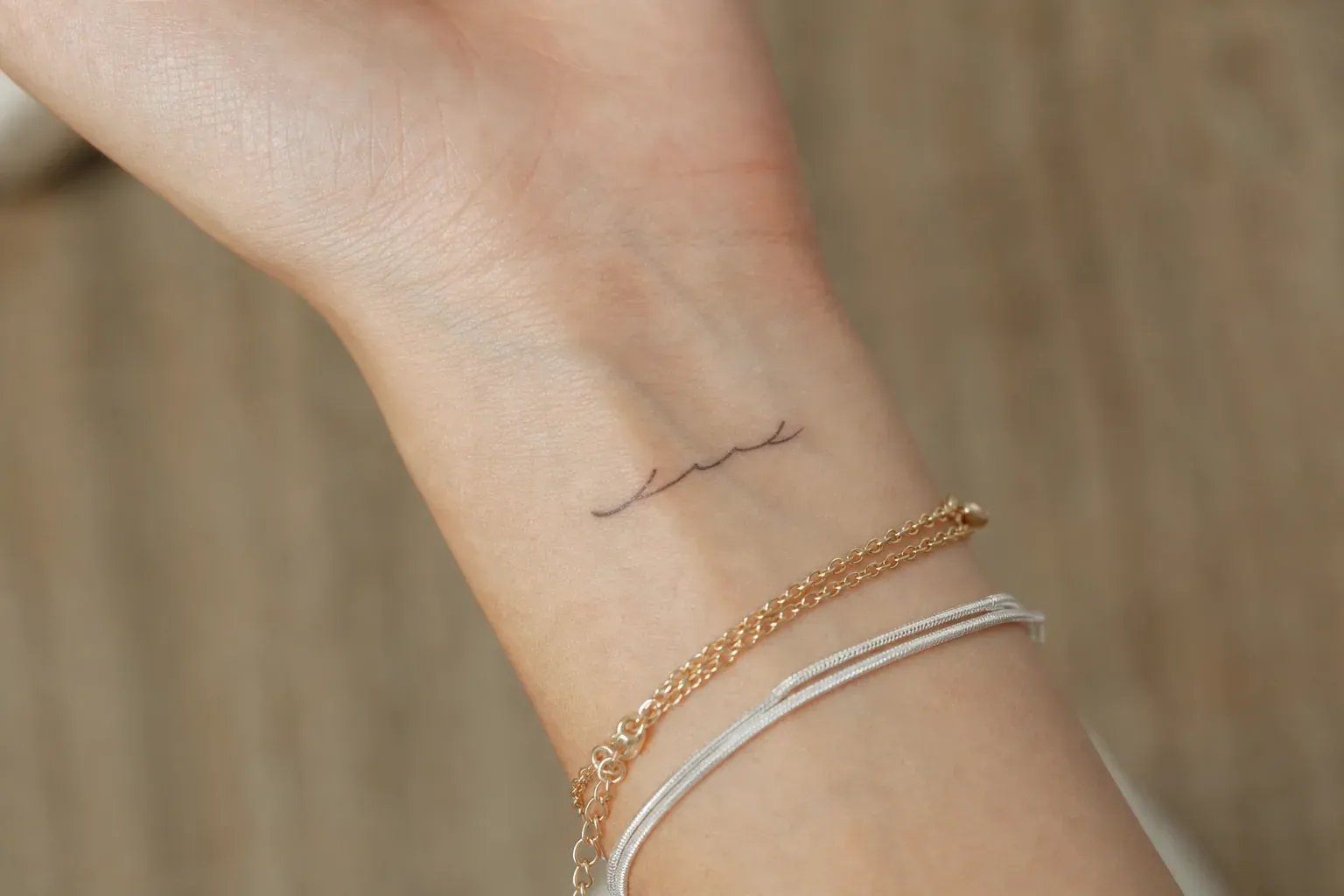 Gros plan réaliste d’un poignet portant un petit tatouage discret de prénom, dans une lumière naturelle douce.